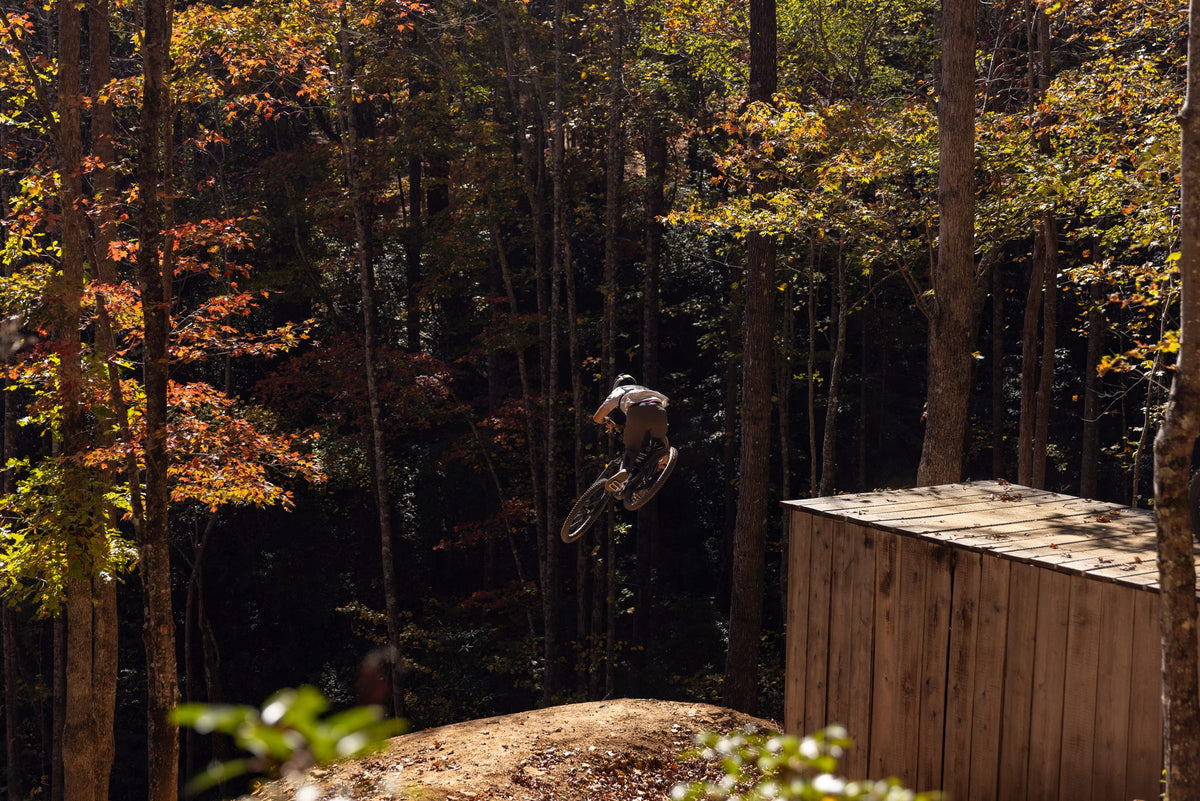Rider jumping a wooden gap in the woods on the Invert Enduro