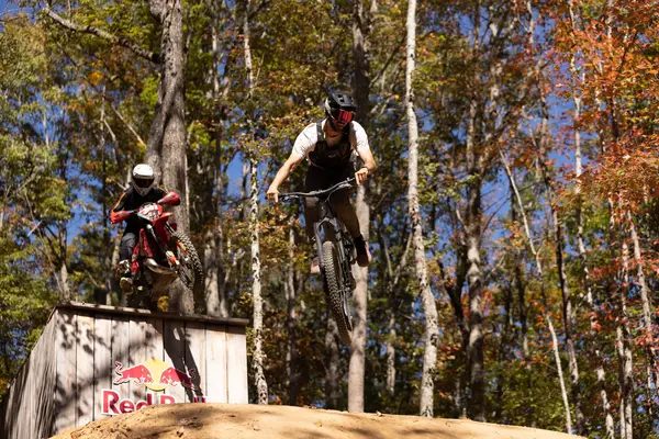 Mountain bike and moto riders airborne off a wooden kicker during filming